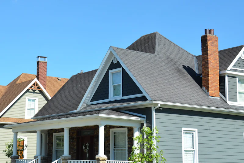 Blue-gray two-story house with a front porch, a brick chimney and a dark shingle roof