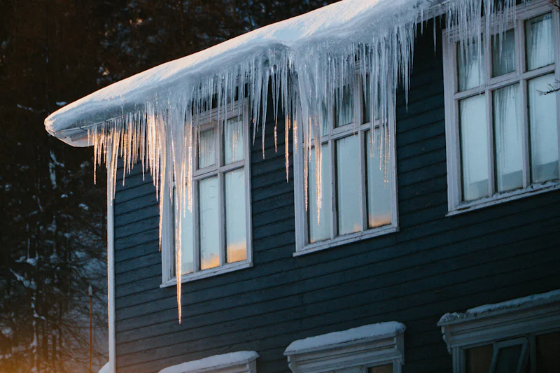 Long icicles hanging from the roof edge of a dark-sided house